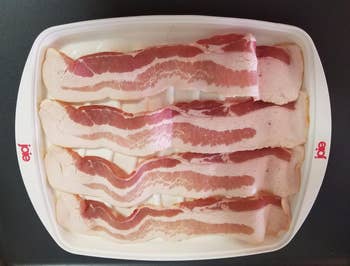 The bacon cooker filled with four pieces of uncooked bacon