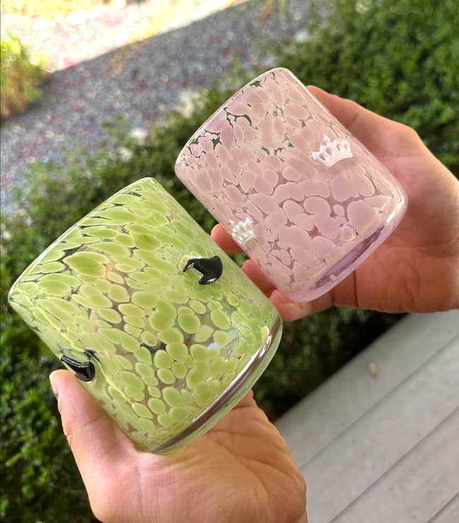 Two hands clasp  colorful, textured solid  tumblers with tiny  crown designs, successful  an outdoor setting