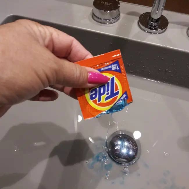 Hand squeezing Tide detergent pack into a sink