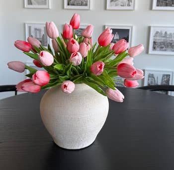 A achromatic  vase with pinkish  tulips arranged connected  a achromatic  array  successful  beforehand   of a assemblage   partition  with framed art