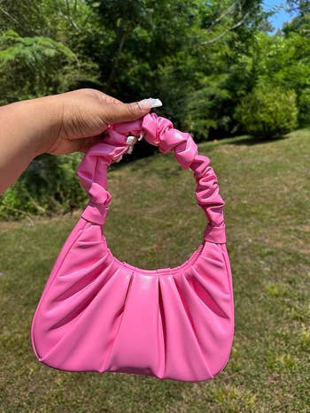 Person holding a small, stylish handbag with gathered detailing, outdoors