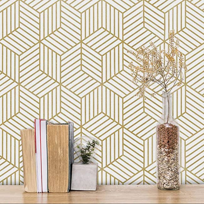 gold geometric patterned wallpaper behind a table with books and plants