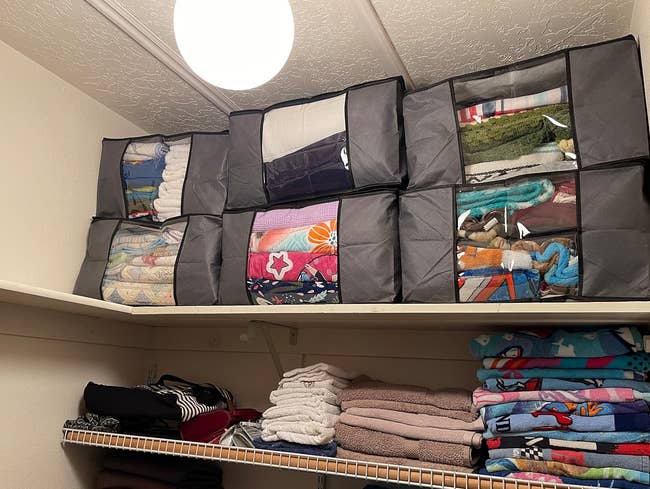 a reviewer photo of six of the bags filled with linens and stacked in a closet 