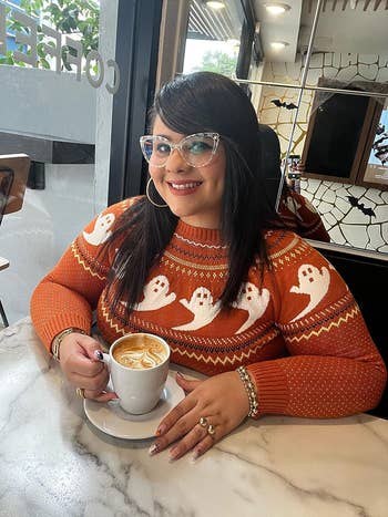 reviewer wearing the orange knit sweater with ghosts on it