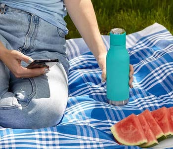 model sitting on a picnic blanket and connecting the water bottle speaker to their phone