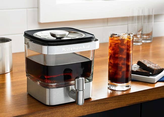 stainless steel cold brew maker next to a glass of iced coffee
