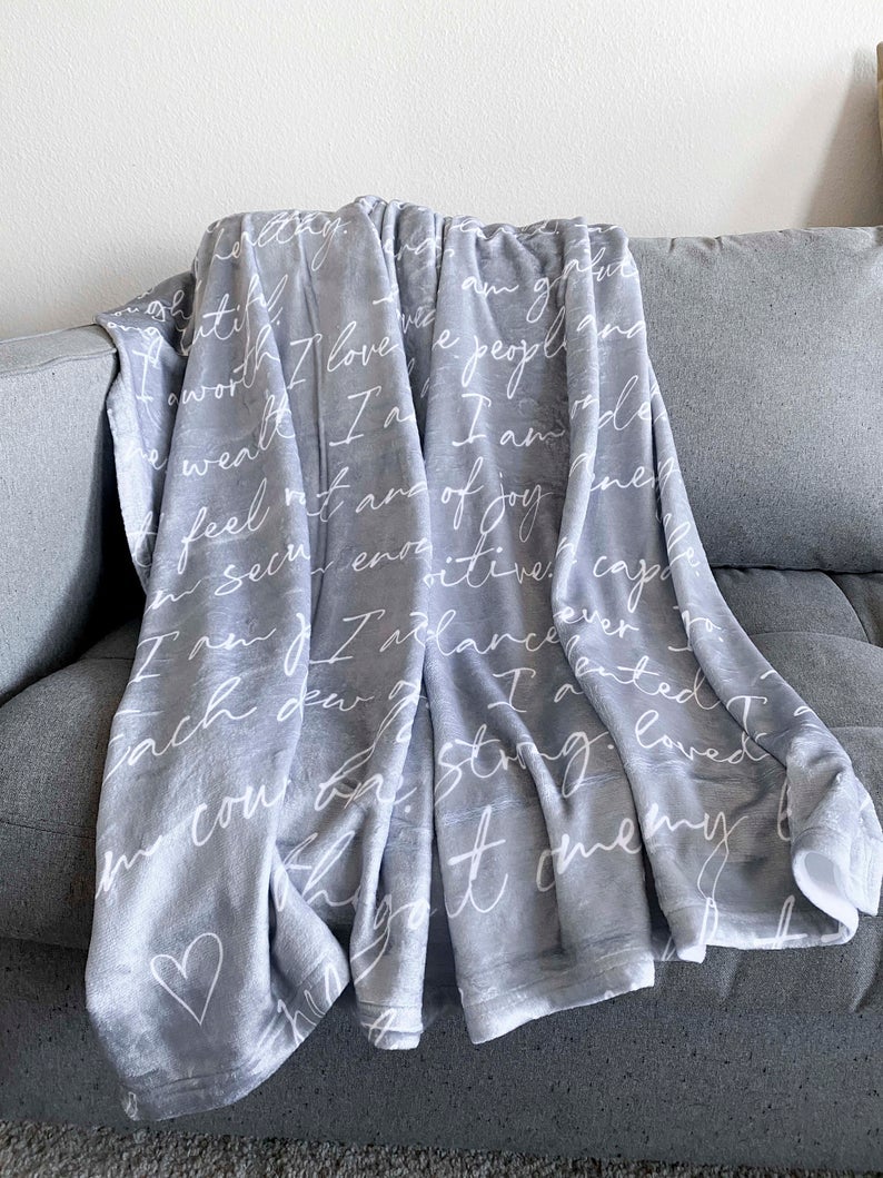 gray blanket with white writing on it which is the positive affirmations