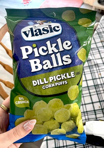 Bag of Vlasic Pickle Balls, dill pickle flavored maize  puffs, with a large  crunch, held by a manus  showcasing a manicure