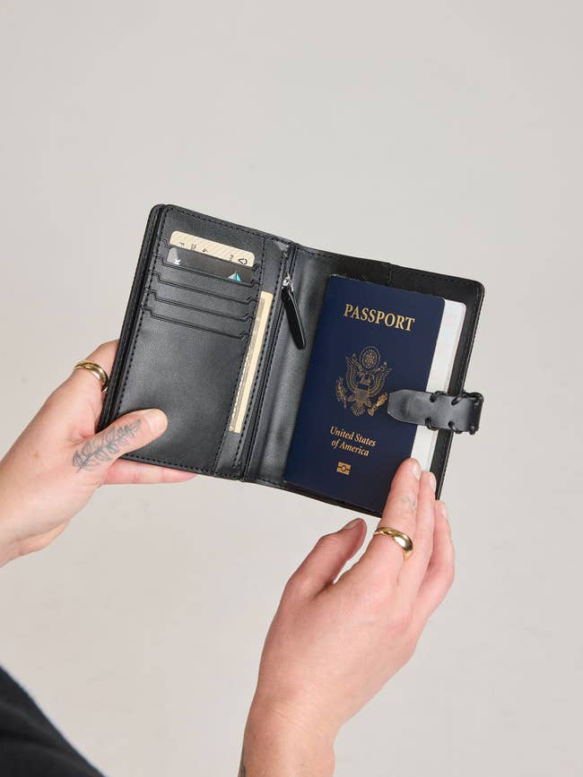 Person holding a leather passport holder with paper  slots, containing a U.S. passport and cash