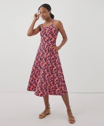 model in a floral patterned, sleeveless, knee-length dress standing in a relaxed pose, wearing strappy sandals