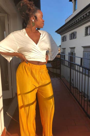 reviewer standing on a balcony wearing yellow pleated palazzo pants