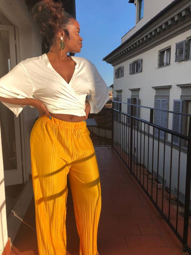 reviewer standing on a balcony wearing yellow pleated palazzo pants