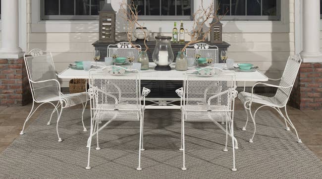 Six white wrought iron patio furniture around a rectangular table outside
