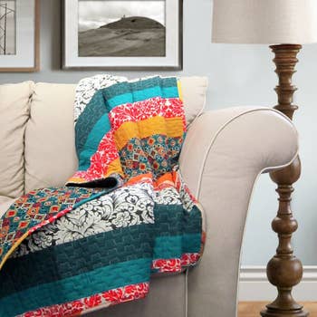Patchwork quilt with geometric and floral patterns draped implicit beige couch; framed creation and lamp successful background