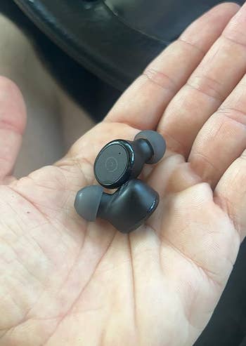 a reviewer holding their black earbuds in their hand
