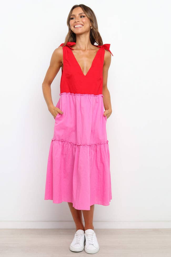 model with hands in pockets of sleeveless tiered dress with red bodice and pink skirt