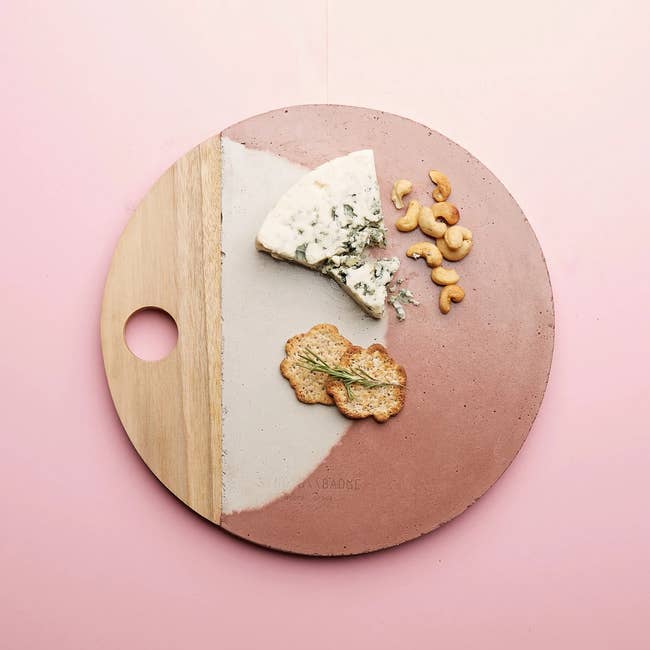 a circular cheese board with a wooden handle and a light grey and burnt orange dyed concrete section