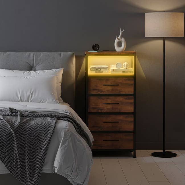 Bedroom with upholstered bed, patterned blanket, a wooden bedside table with books, clock, lamp, and decorative antler, and a standing lamp