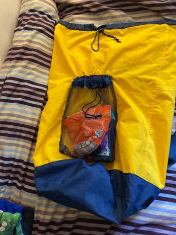 Yellow drawstring container  with a smaller mesh pouch holding colorful snack bags, placed connected  a striped bedspread