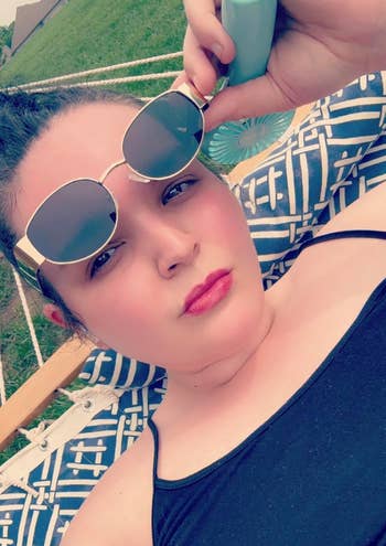 Person lying connected  a patterned hammock, wearing sunglasses and holding a bottle
