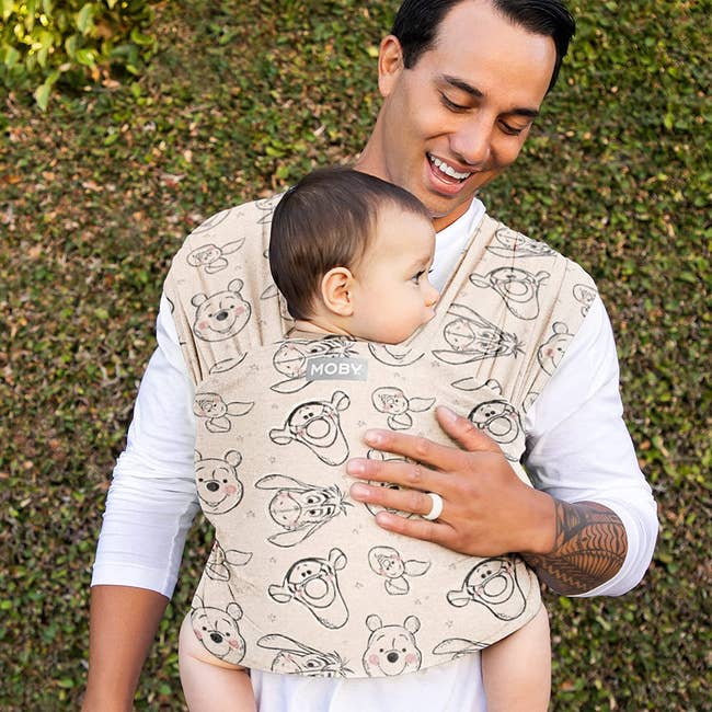 a parent wearing the tan moby wrap with winnie the pooh characters on it