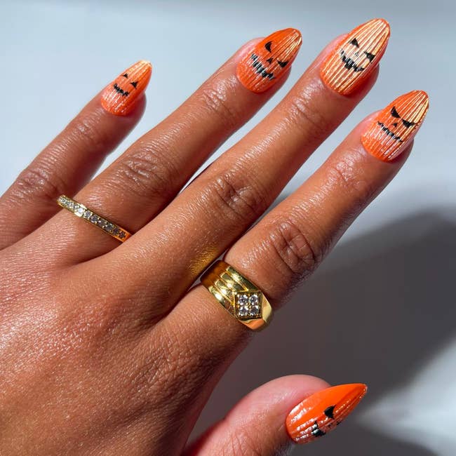 Hand showcasing pumpkin-themed Halloween nail creation with golden rings