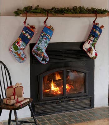 three l.l. bean needlepoint stockings hung by a fire