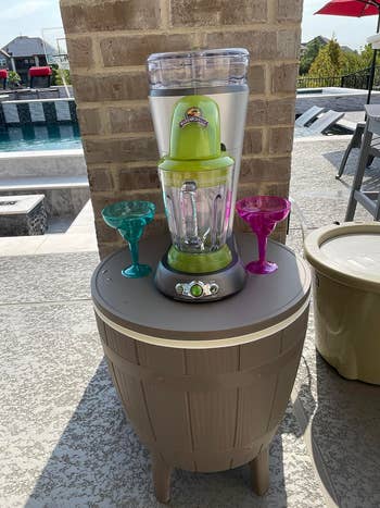 Blender with greenish pitcher and 2 colorful margarita glasses connected a patio adjacent a pool, cleanable for outdoor summertime entertaining