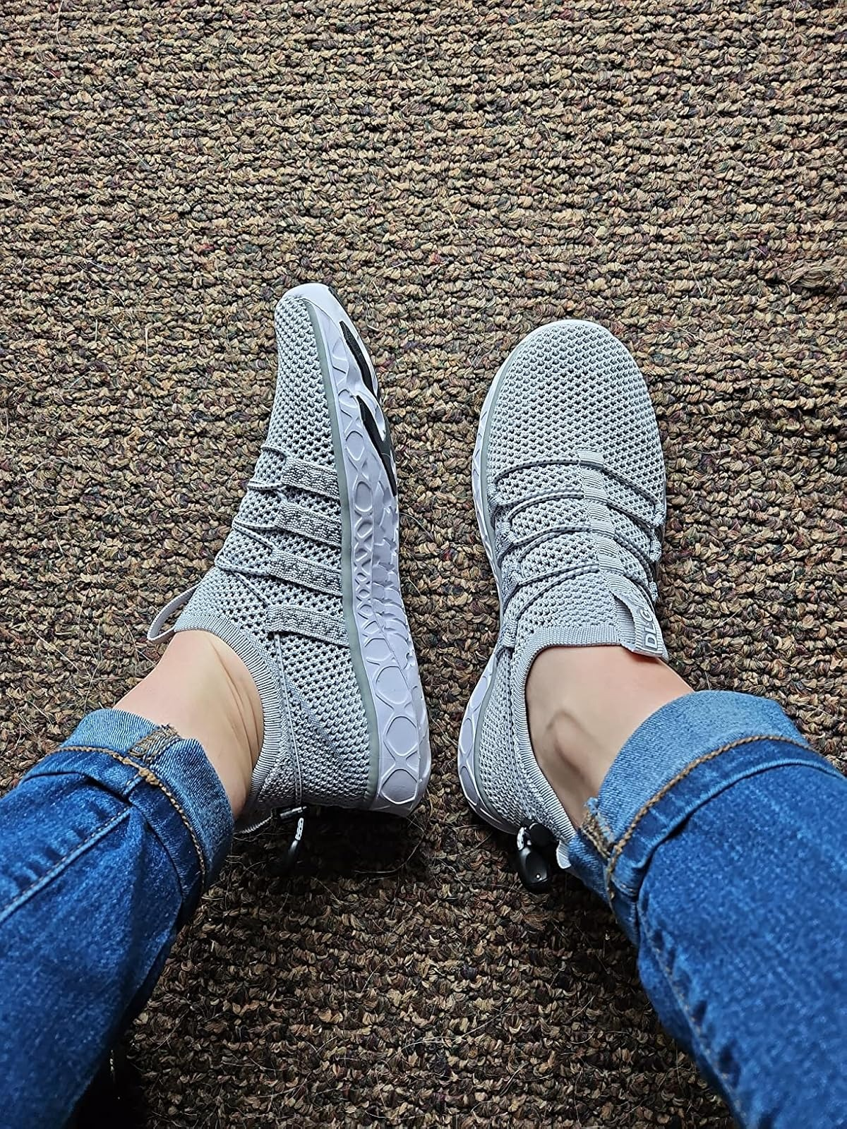 A reviewer wearing bluish  jeans and a brace  of gray, textured sneakers with a unsocial   sole signifier   connected  a carpeted floor