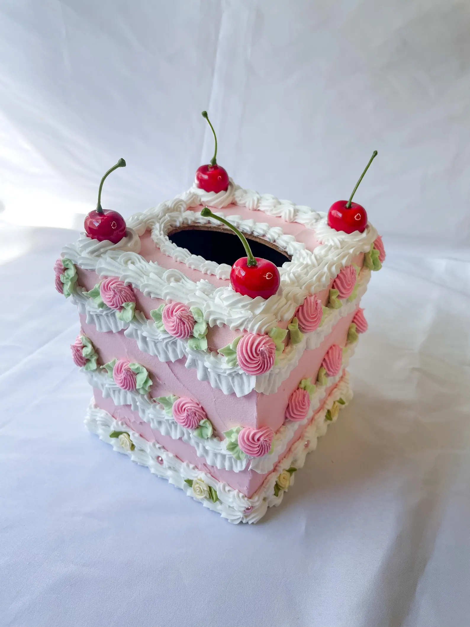 Decorative cake-style insubstantial   container  holder with pinkish  frosting plan  and cherry accents connected  top, evoking a sweet, whimsical appearance