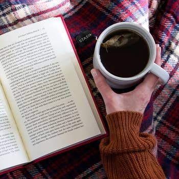 Person holding a mug of beverage  adjacent  to an unfastened  book, resting connected  a plaid blanket. Perfect mounting  for cozy speechmaking  time