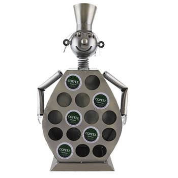 Metallic coffee pod holder shaped like a chef with cup slots, holding various pods. Ideal for organizing coffee essentials stylishly