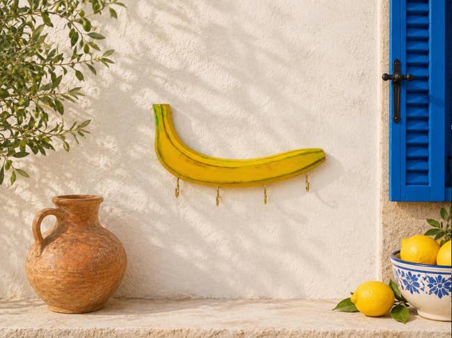 Wall hanging shaped similar  a banana with hooks, acceptable   adjacent  to a ceramic jug and lemons successful  a vessel  connected  a sunny outdoor shelf