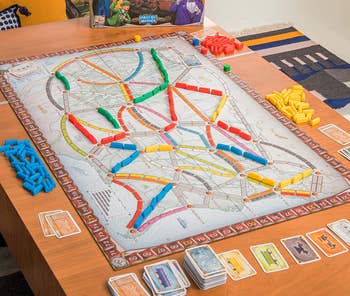 a table with the game board, playing cards and train car pieces set up 