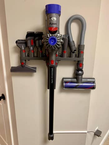 Reviewer's dyson stick vacuum hanging in attachment holder on wall (not included) with attachments