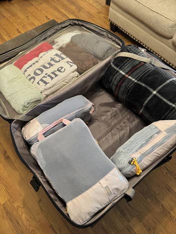 Open suitcase with neatly packed clothes, including packing cubes, a plaid blanket, and a sweater. Ideal for question organization