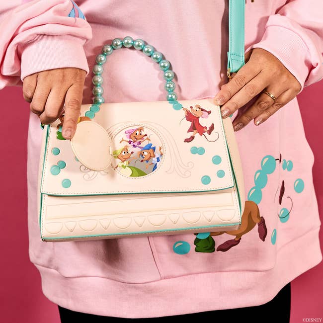 a model holding a folded over handbag with the mice from cinderella on it stringing beads that then form the bag's handle