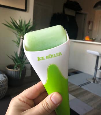 Hand holding an ice roller skincare tool with a green and white handle