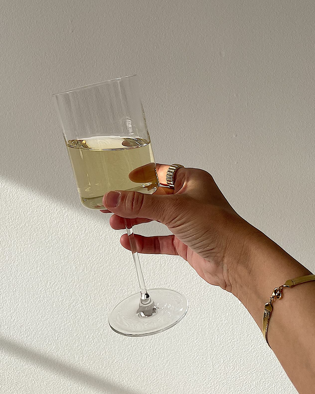 Hand holding a glass of white wine against a neutral background, highlighting the elegant design of the wine glass
