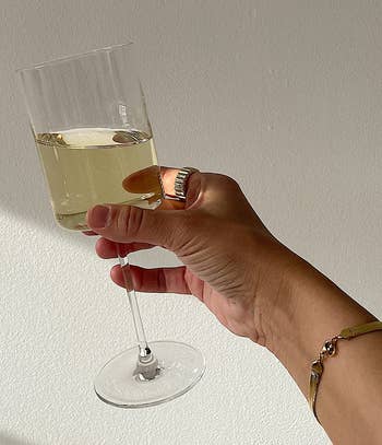Hand holding a glass of white wine against a neutral background, highlighting the elegant design of the wine glass
