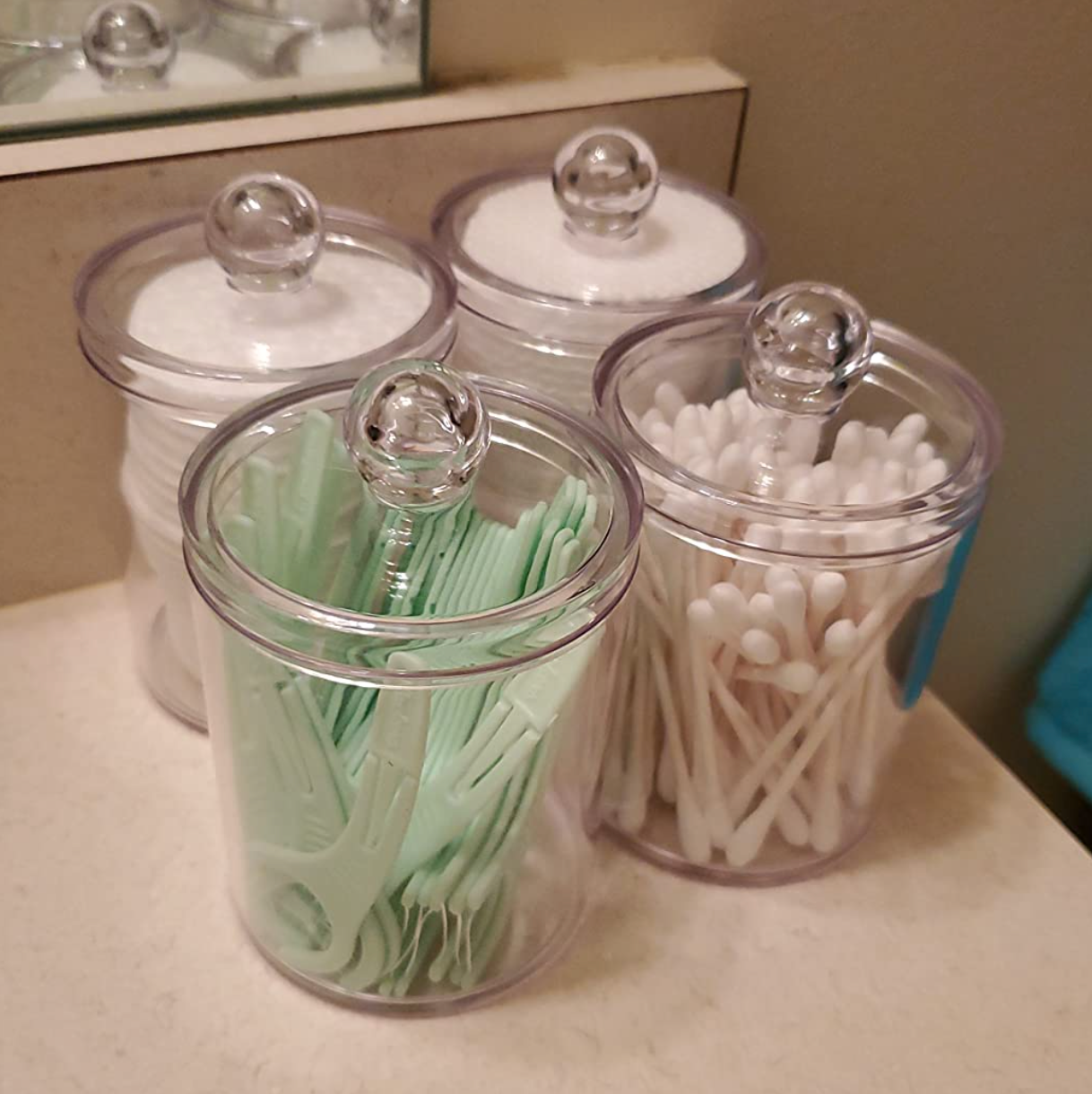 Four small clear cylinder shaped canisters with swabs and flossers in them 