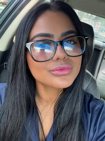 Person successful  a car   wearing oversized glasses and a dark-colored top, looking into the camera with a neutral expression