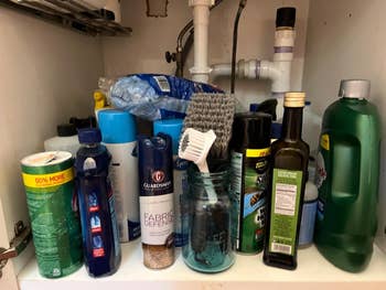 A variety of cleaning supplies and products, including sprays, bottles, and brushes, are stored in a cabinet under the sink
