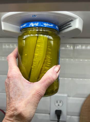 reviewer holding jar of pickles up to opener device