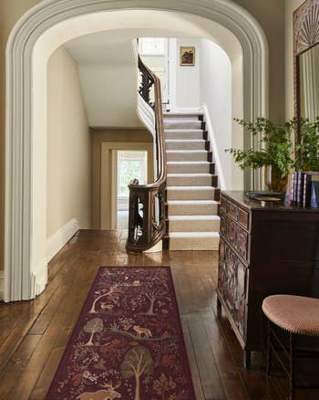 Elegant hallway with intricate woody  staircase, vintage-style chest, and nature-themed carpet runner, starring  to a sunlit precocious    floor