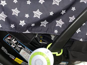 A portable white noise machine attached to a baby car seat with star-patterned canopy