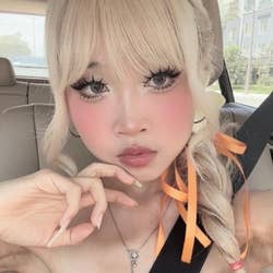 Person in a car with long eyelashes, braided hair with ribbons, and delicate makeup, wearing a necklace