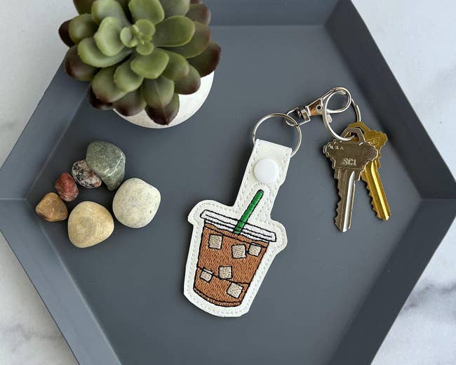 Keychain with iced java  plan  adjacent  to keys, tiny  rocks, and a succulent connected  a tray