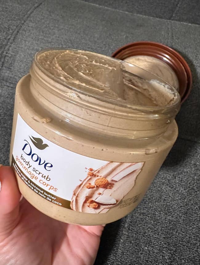 Open jar of Dove assemblage  scrub with disposable   creamy texture, labeled to incorporate  crushed macadamia and atom   milk