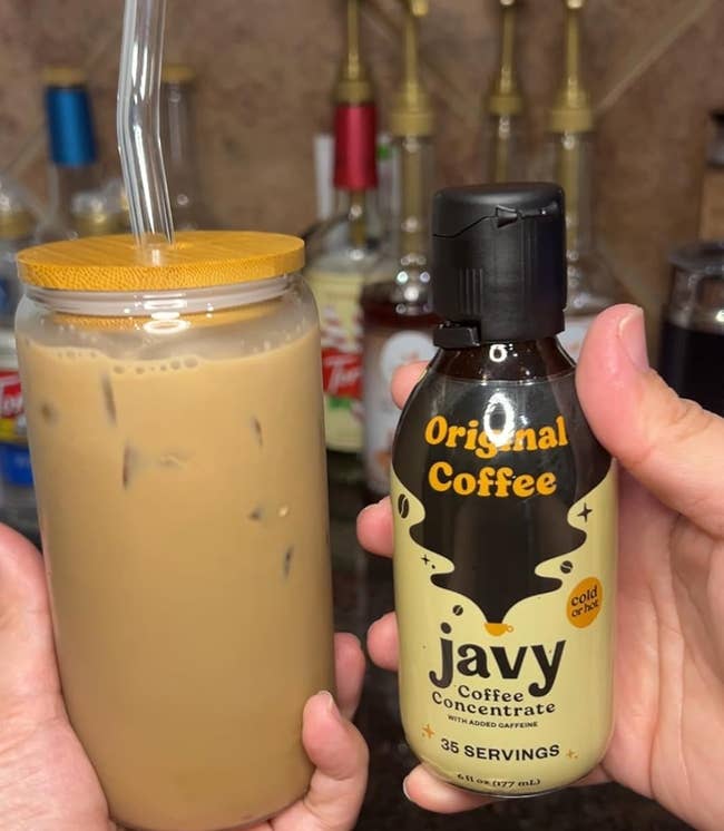 Hand holding a bottle of Javy Coffee Concentrate next to an iced coffee drink in a mason jar with a straw
